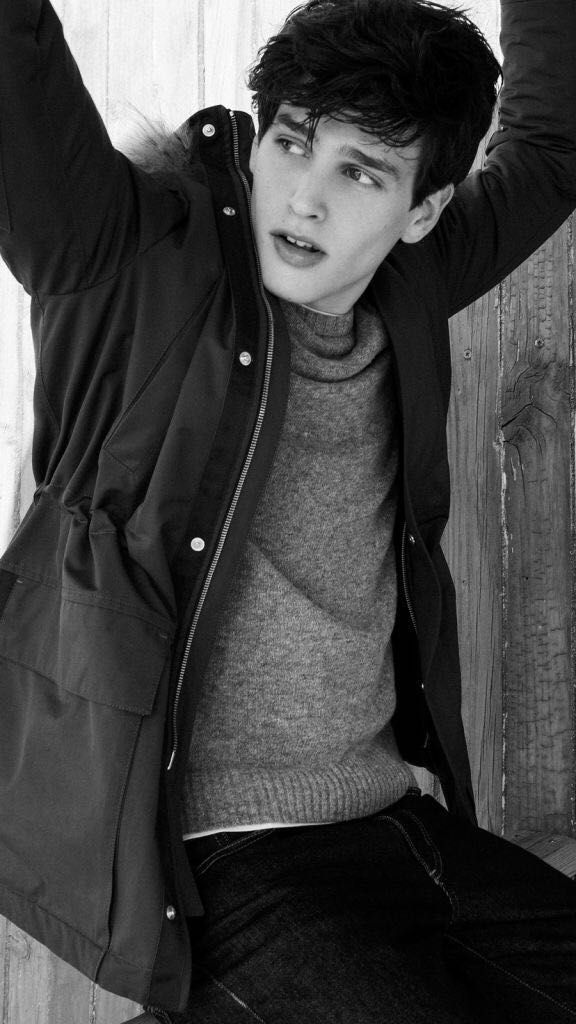 a young man leaning against a wooden wall with his hands on his head and looking at the camera