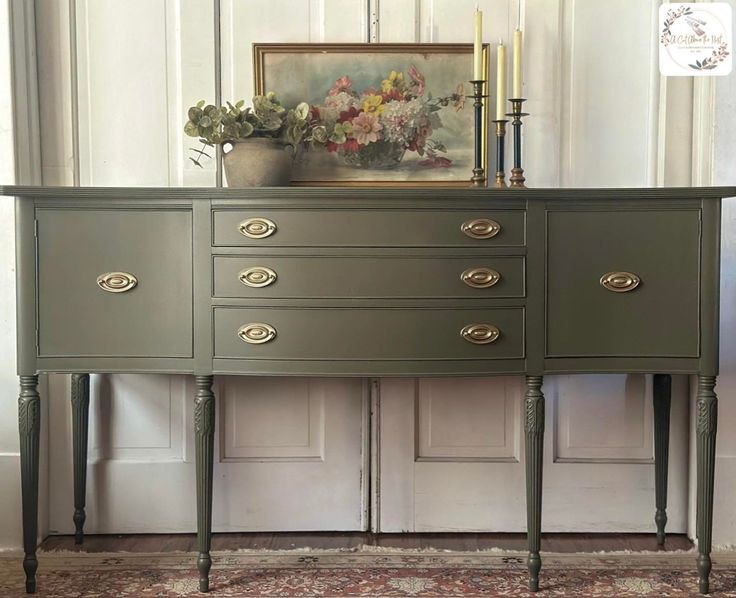 a green dresser with gold handles and drawers in front of a painting on the wall