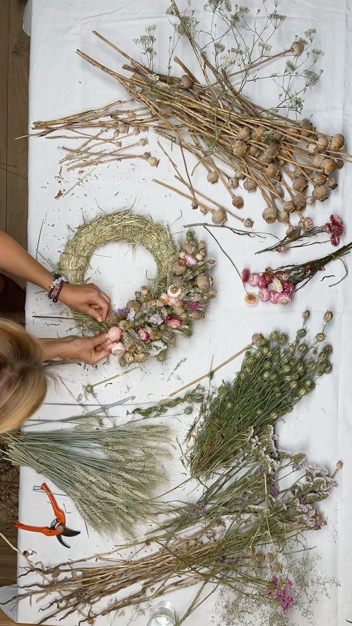 the woman is working on her craft with dried flowers and plants in front of it