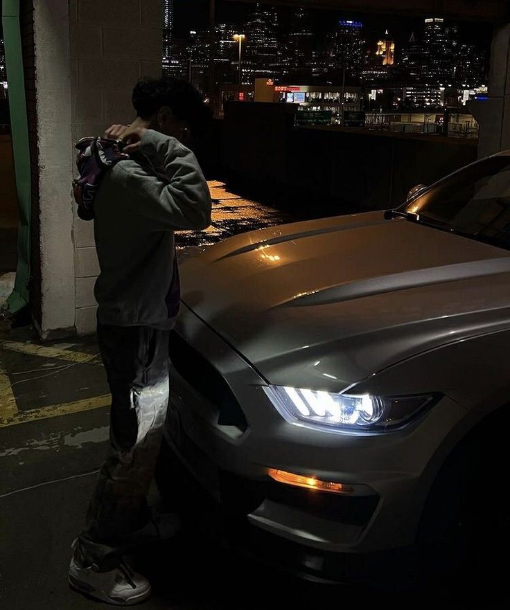 a man standing next to a silver car in the dark with his hands on his face