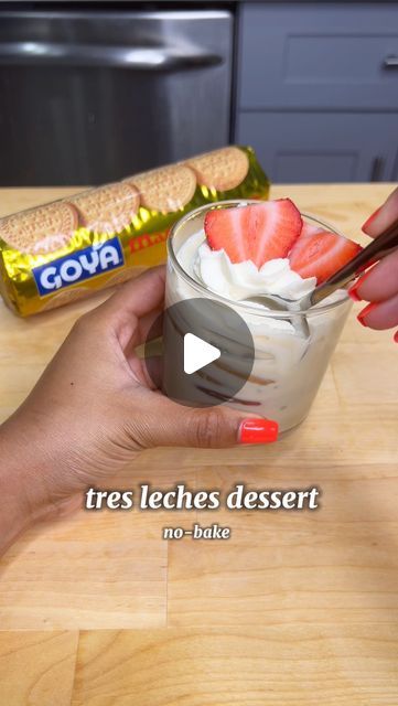 a person holding a spoon over a dessert in a glass on top of a wooden table