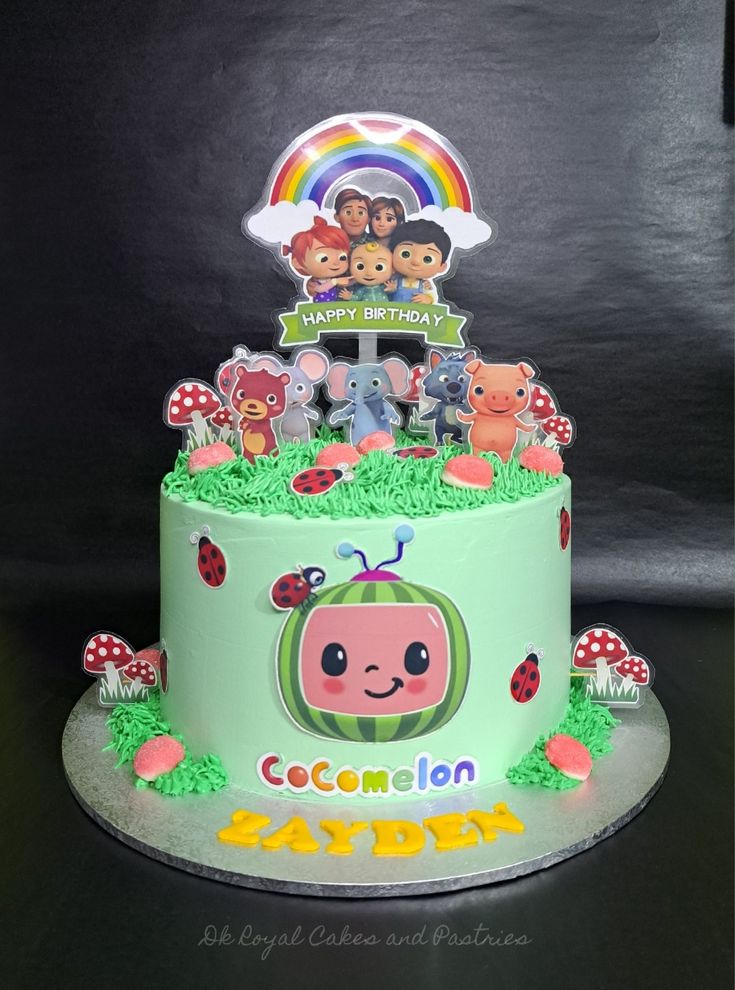 a birthday cake decorated with cartoon characters and decorations on top of a green base that says cocomelon bayden