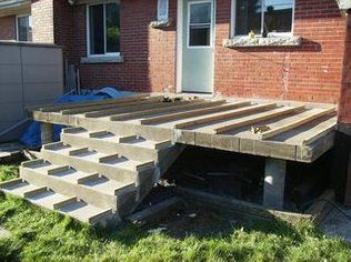 an outdoor patio being built in front of a brick house with steps leading up to it