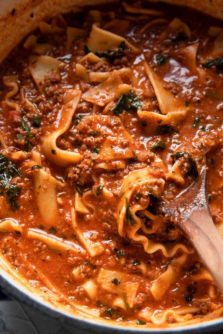 a large pot filled with pasta and meat sauce on top of a wooden spatula