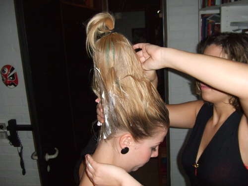 two women blow drying their hair in a room with books on the wall behind them