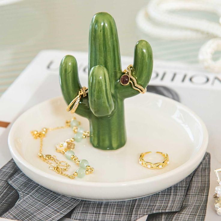 a green cactus sitting on top of a white plate next to some gold bracelets