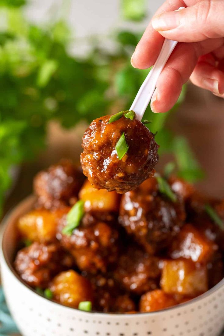 a hand holding a ladle full of meatballs and garnished with cilantro