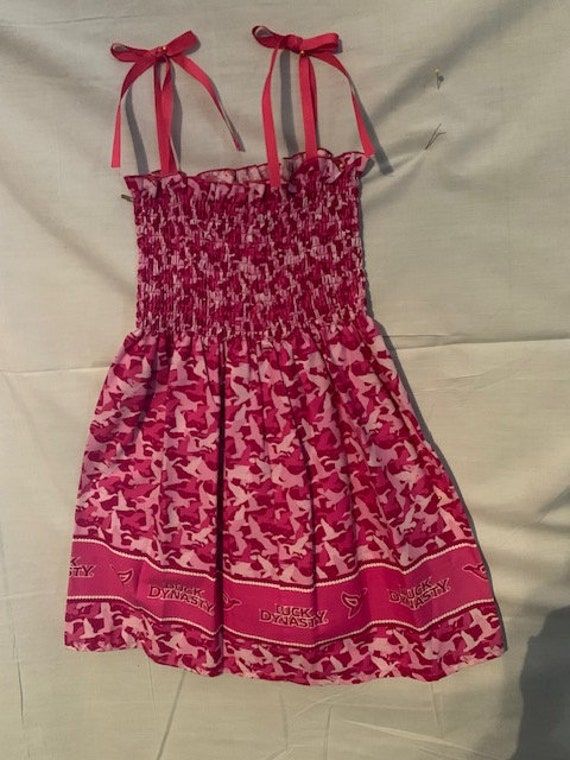 Duck Dynasty Smocked sundress with the duck dynasty print on the border of the dress and tie ribbon  straps. Pink Sundress With Ruffled Straps For Beach, Sleeveless Smocked Dress With Tie Straps For Summer, Cotton Sundress With Smocked Bodice For The Beach, Sleeveless Smocked Sundress With Elastic Neckline, Casual Sundress With Tie Back And Ruffled Straps, Casual Sundress With Ruffled Straps And Tie Back, Sundress With Tie Back And Ruffled Straps, Cotton Sundress With Smocked Bodice, Lined Smocked Sundress For Summer