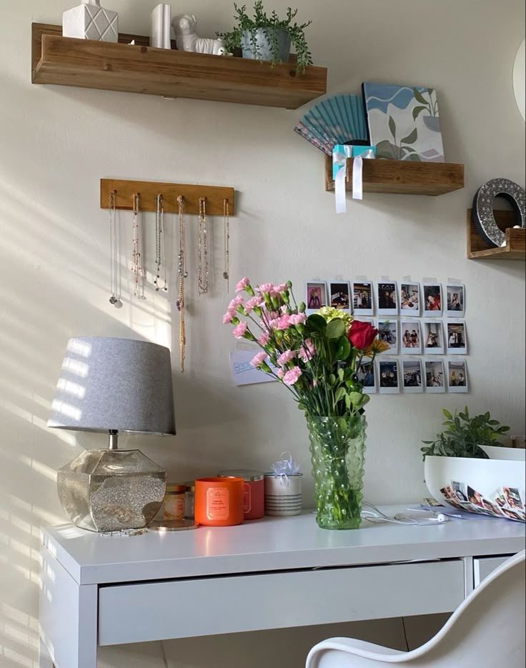 a white desk topped with a vase filled with flowers next to a wall mounted fan