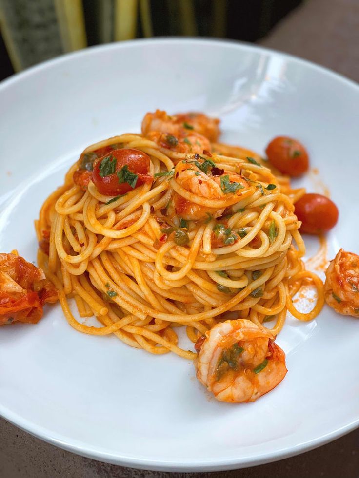 pasta with shrimp and tomato sauce on a white plate, ready to be eaten by someone