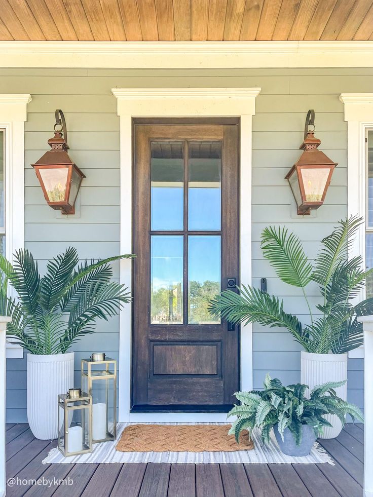 the front door of a house with potted plants and two lanterns on the porch