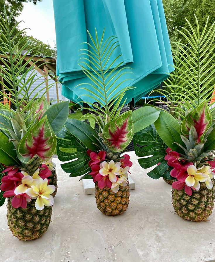 three pineapples with flowers and leaves in them on a table next to some plants