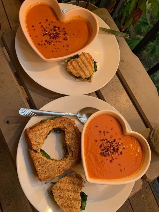 two white plates topped with heart shaped sandwiches next to soup and dipping sauce on top of each other