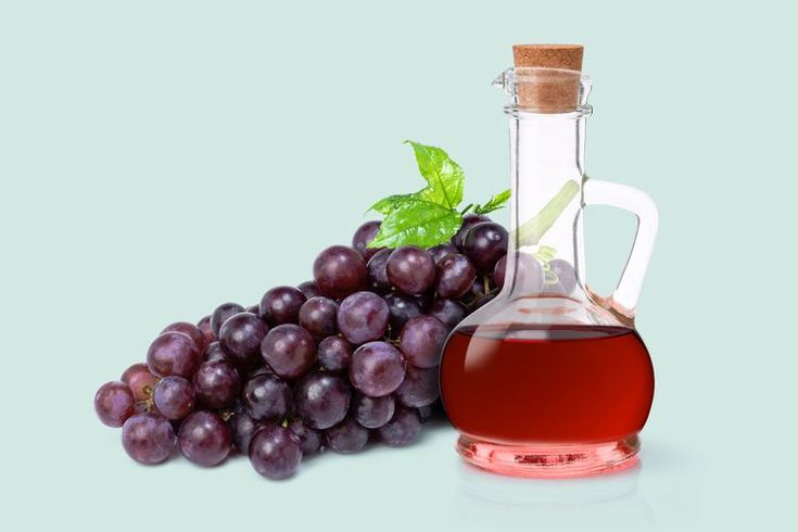 grapes next to a bottle of liquid on a blue background