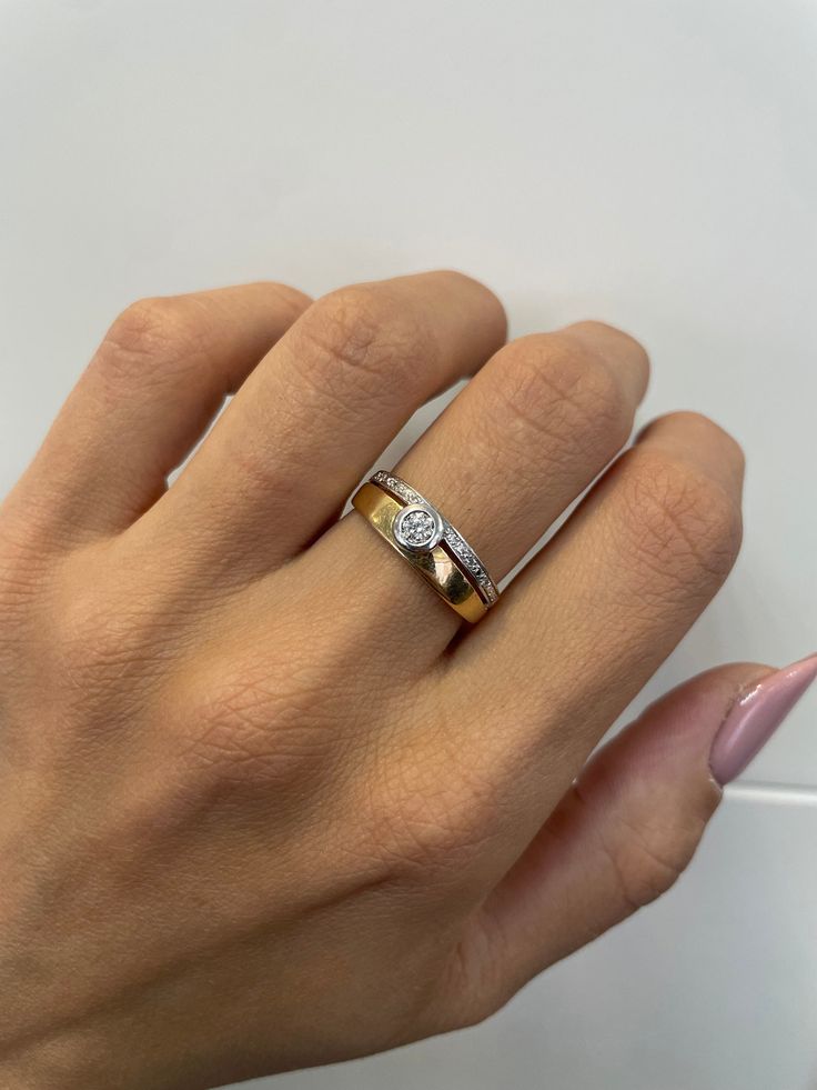 a woman's hand with a gold and white ring on her left hand, holding a pink manicure