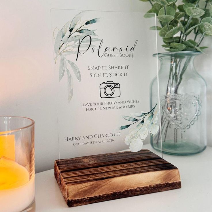 a clear glass vase with flowers and candles on a table next to a sign that says polaroid guest book