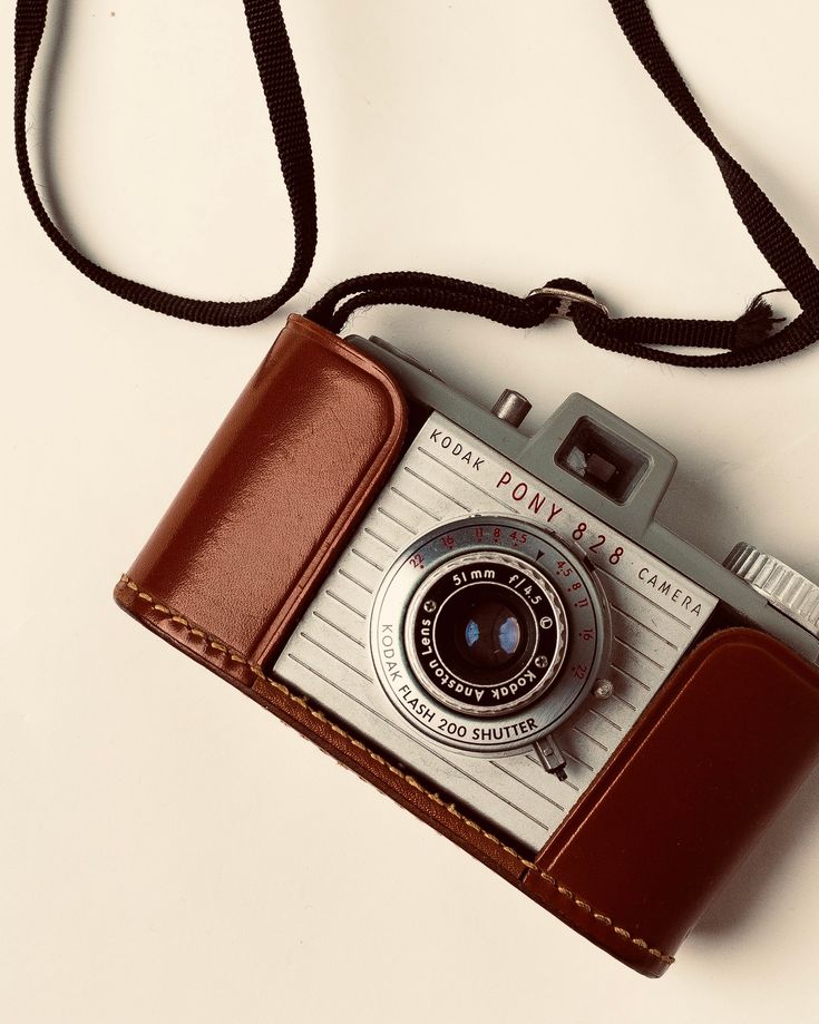 an old fashioned camera sitting on top of a brown leather case with a black strap