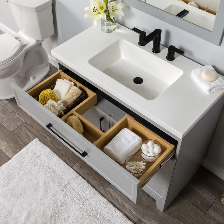 a bathroom with a sink, mirror and toiletries in the cabinet drawer open to show its contents