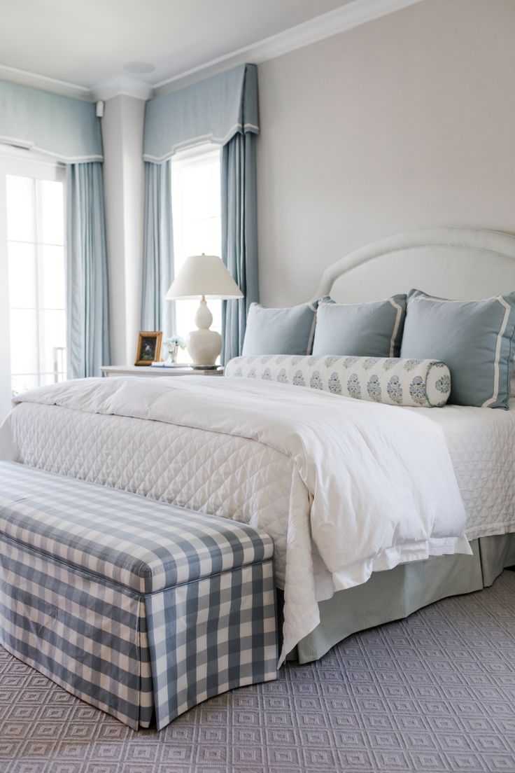 a white bed sitting in a bedroom next to a window filled with blue and white curtains