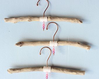 three pieces of driftwood hang from hooks on a blue wall with pink bead string