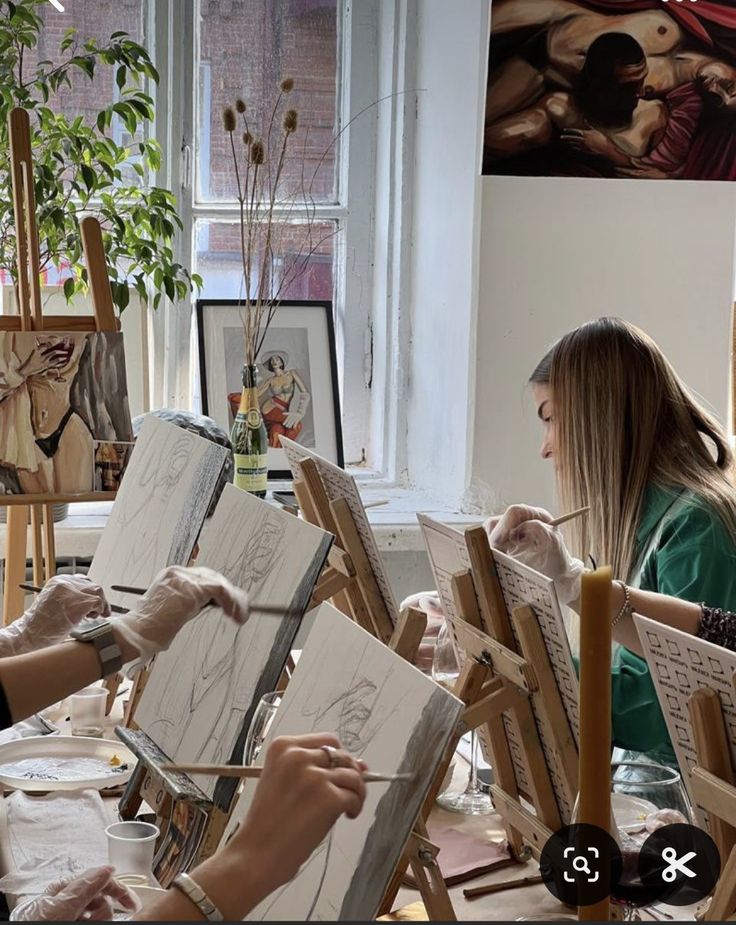 two women are painting in an art studio with easels and paintings on the walls