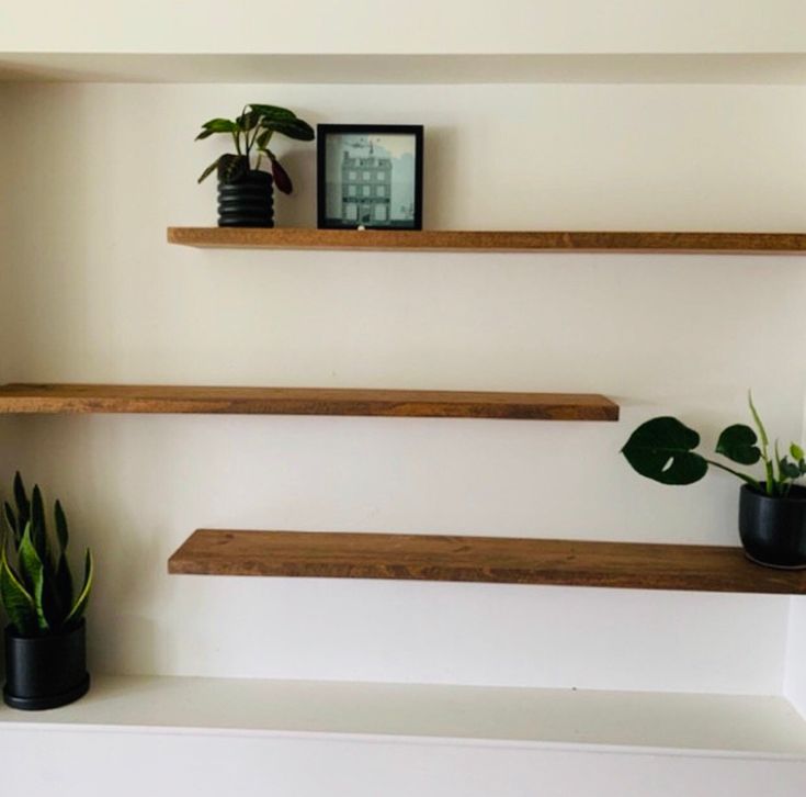 three wooden shelves with plants on them in a living room or dining room, one is empty and the other has two potted plants