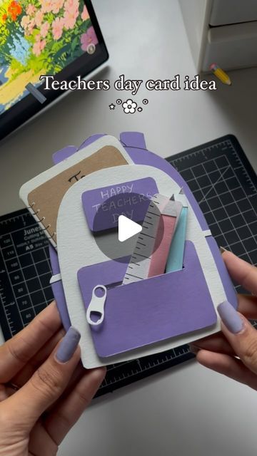 a person holding up some crafting supplies on a table with a computer in the background