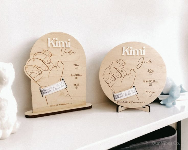 two wooden plaques with hand prints on them sitting next to a teddy bear and stuffed animal