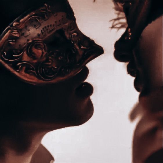 two people with masks on their faces are facing each other and one is kissing the other