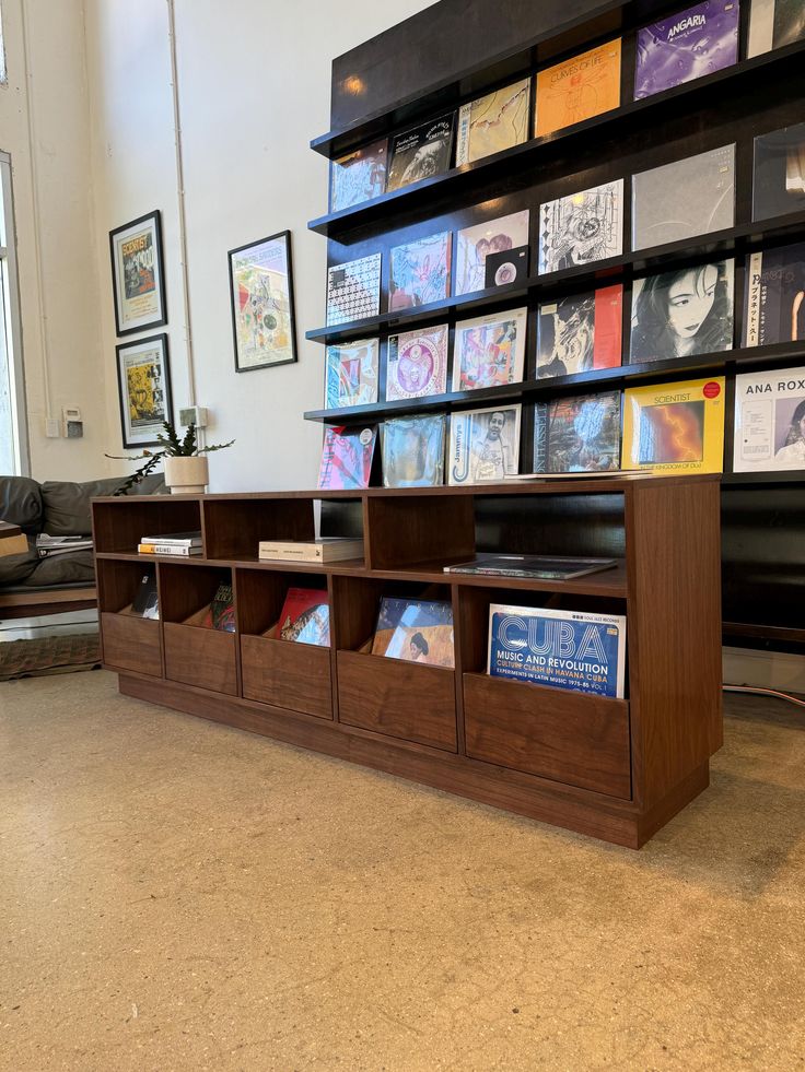 a bookshelf filled with lots of books in front of a wall full of pictures