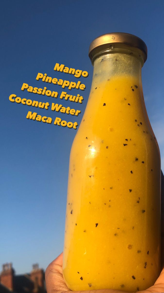 a hand holding up a glass bottle filled with fruit and vegetables, labeled mango pineapple passion fruit coconut water maca root