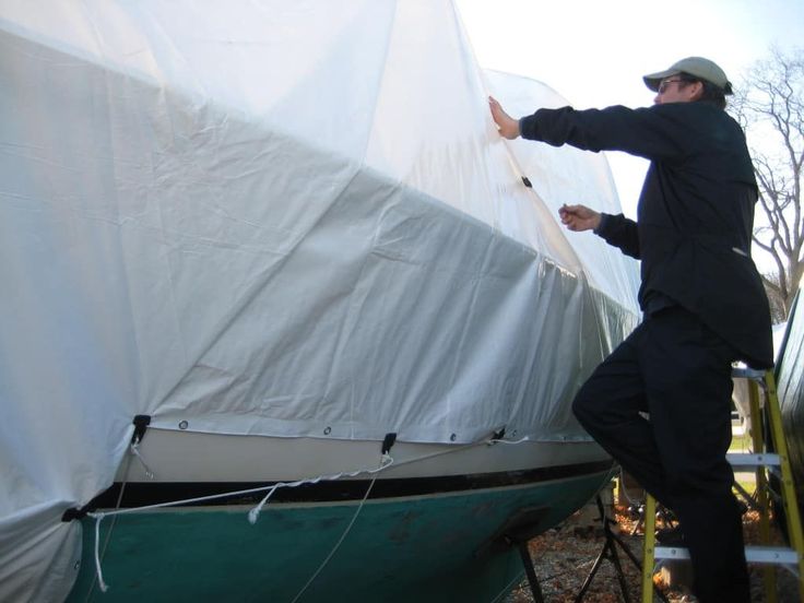 a man standing next to a boat covered in white tarp