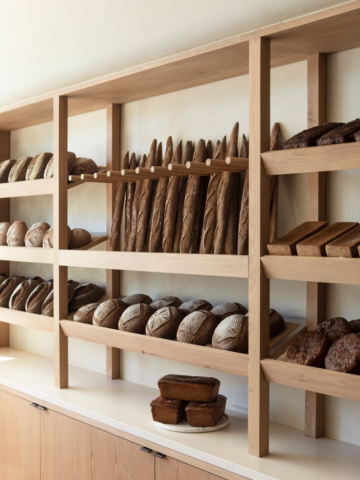 breads and pastries are displayed on shelves in a bakery shop, with white walls