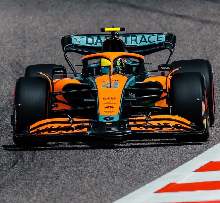 a man driving a race car on a track with an orange and black front tire