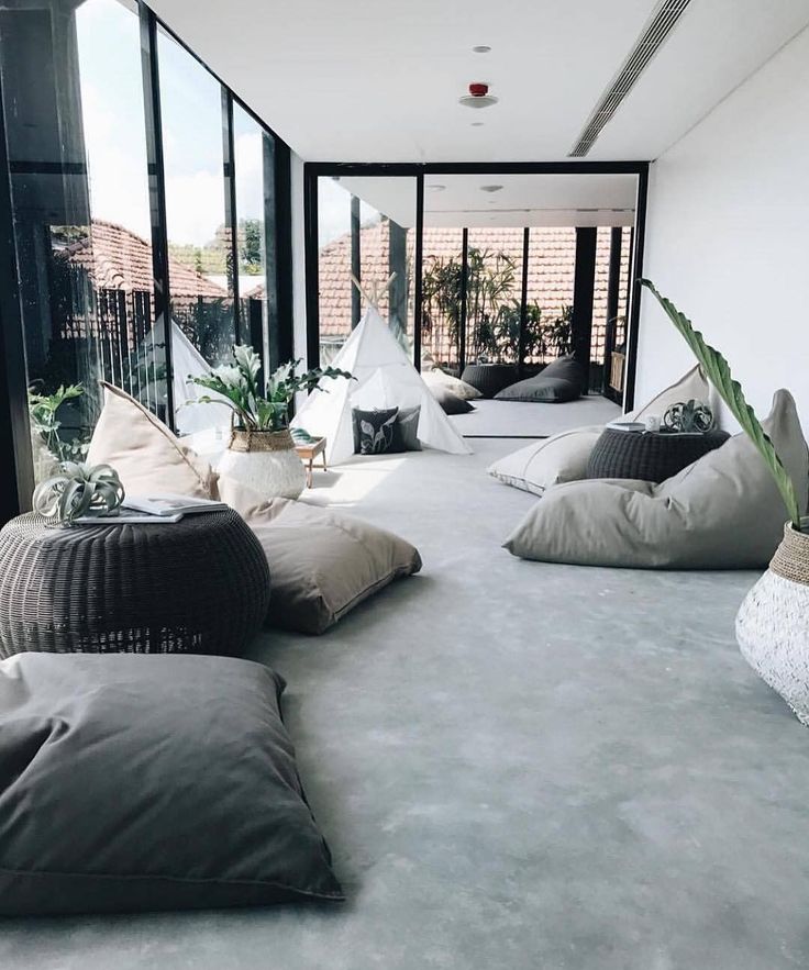 a living room filled with lots of pillows on top of a gray floor next to large windows