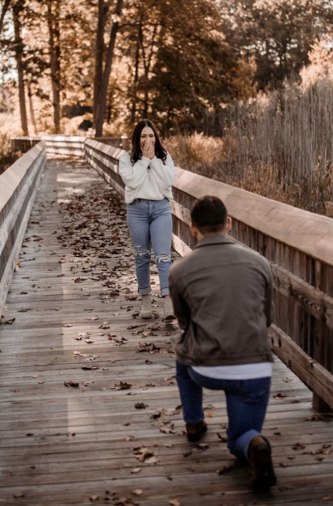 a man and woman walking across a wooden bridge in the fall with leaves on the ground