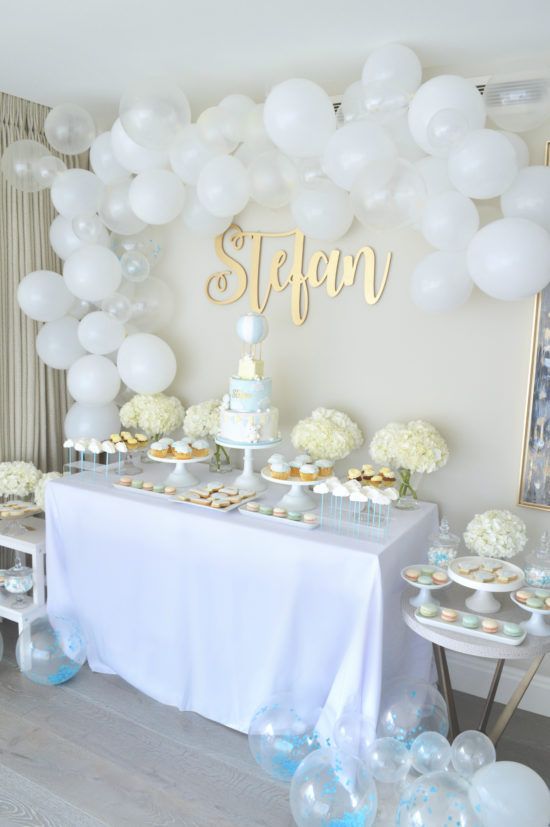 a table topped with lots of white balloons and cupcakes next to a cake