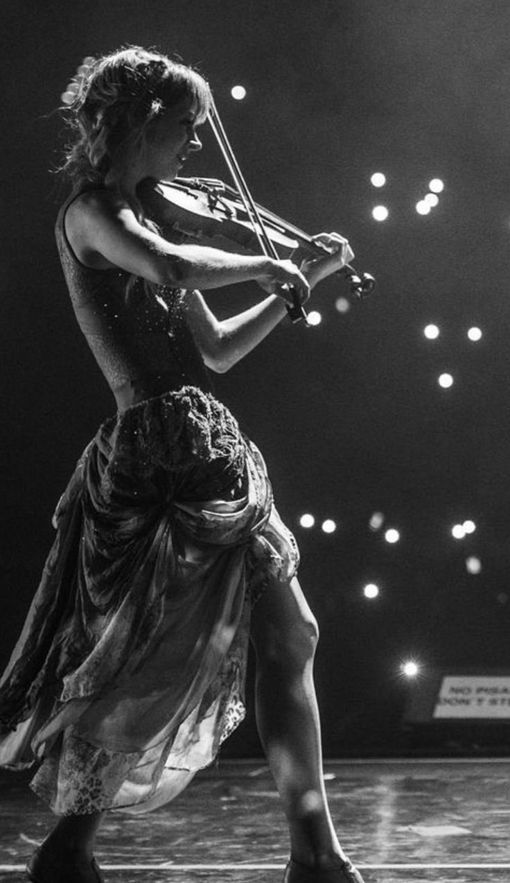 a woman in a dress playing the violin on stage with lights above her and behind her