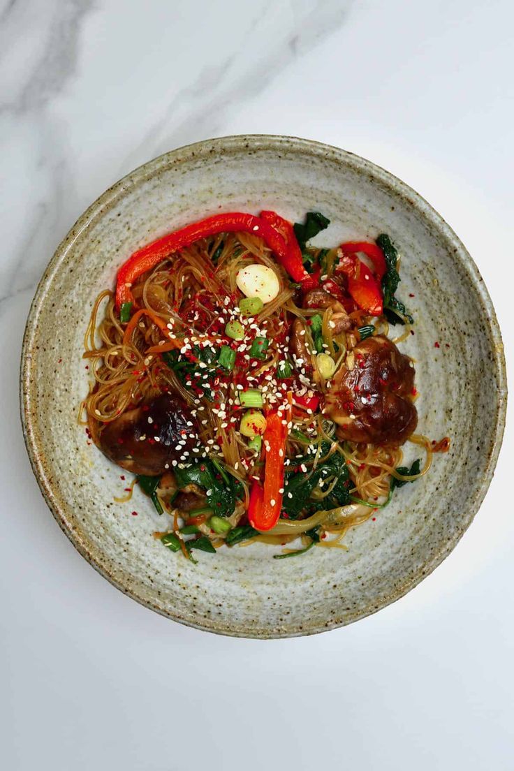 a bowl filled with noodles and vegetables on top of a white countertop next to a fork