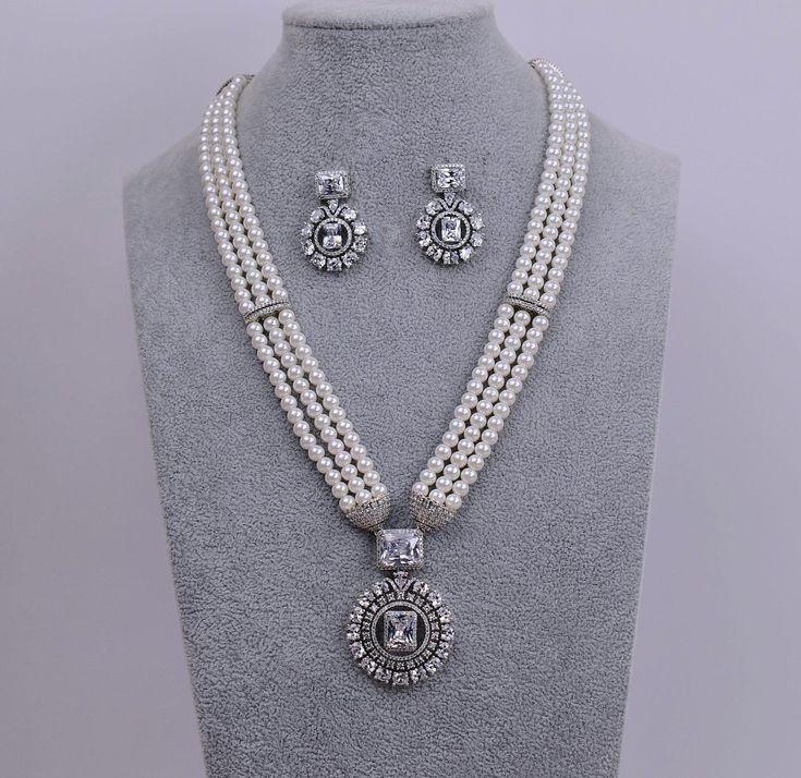 A Swarovski necklace set in premium quality white pearls exudes luxury and elegance, making it the perfect choice for any occasion. Necklace Length: 12.5" with adjustable chain Earrings Push-Back closure. Earring Lenght: Studs 1.25" Sterling Silver finish on high-quality brass as a base metal. Availability: In-Stock. *Color may vary slightly due to light condition & photography. Jewelry Care:  Keep away from moisture. Allow perfumes and lotion to dry before wearing. Store in jewelry pouch. Clean Luxury White Jewelry With Channel Set, Luxury Cubic Zirconia Jewelry With Pearl Chain, Luxury Silver Kundan Necklace For Party, Luxury White Pearl Chain Jewelry Set, Luxury Silver Kundan Necklace For Wedding, Luxury Temple Jewelry Pearl Necklace For Party, Luxury Temple Jewelry Cubic Zirconia Necklaces, Luxury Silver Kundan Jewelry Sets, Luxury Silver Temple Necklace For Festive Occasions