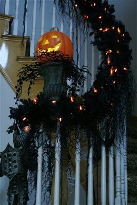 a halloween wreath with pumpkins and lights on the front porch stair railing for decoration