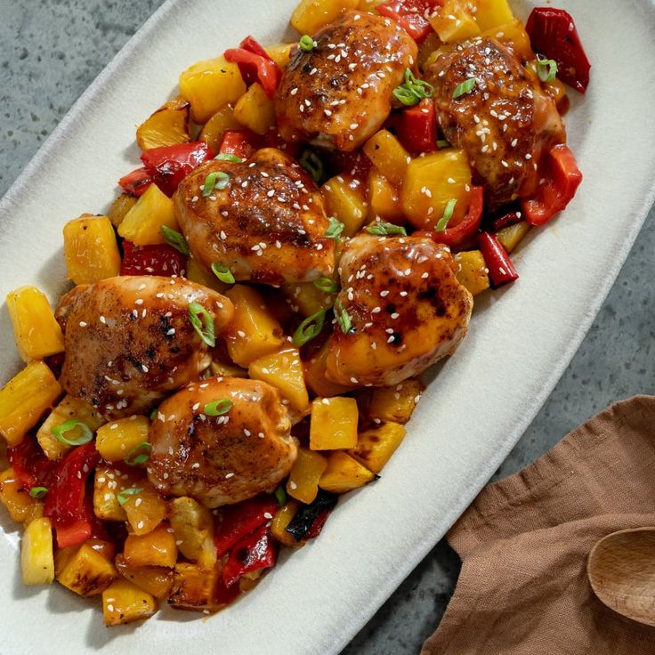 a white plate topped with meat and pineapples on top of a table next to a wooden spoon