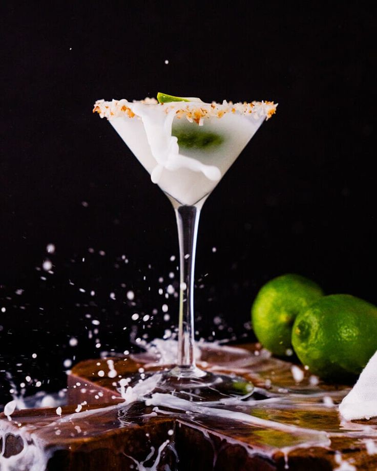 coconut martini with limes and whipped cream on the rim, in front of a black background