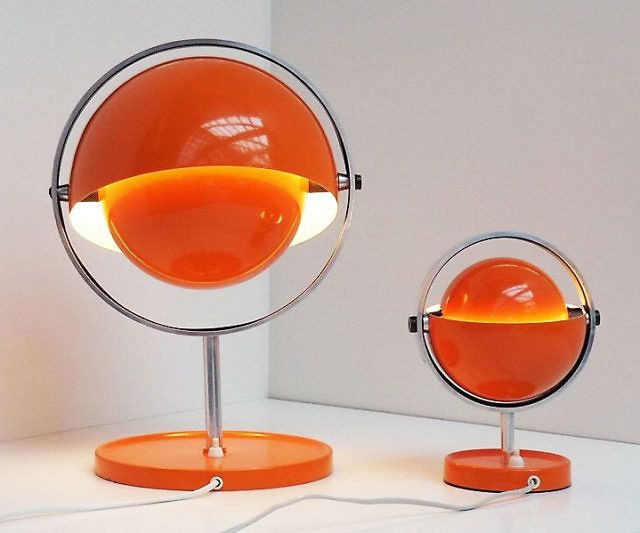 an orange lamp sitting on top of a table next to a round mirror with a light bulb