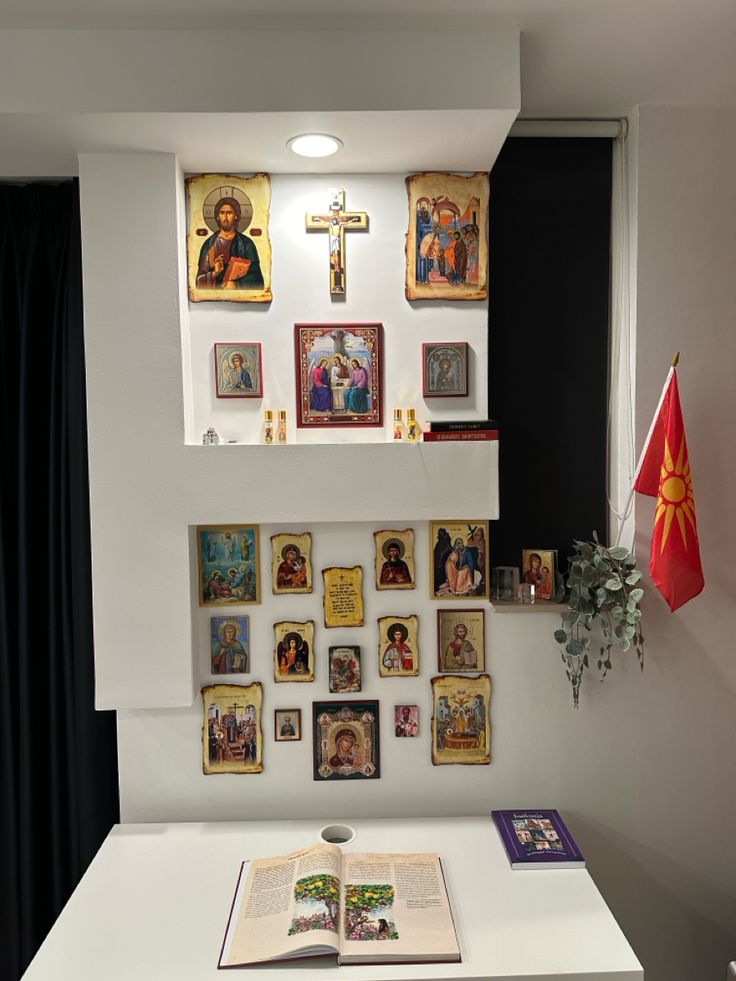 an open book sitting on top of a white table in front of a wall covered with pictures