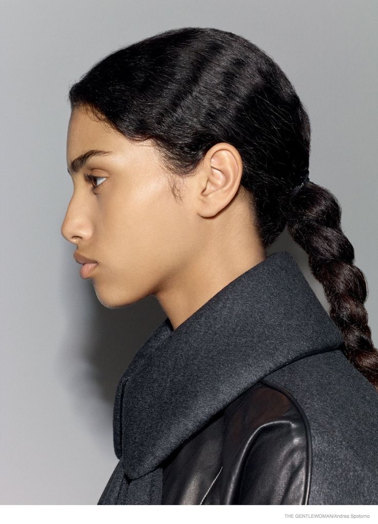 a woman with braids in her hair wearing a black coat and leather jacket against a gray background