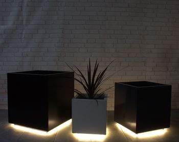 three black square planters lit up with leds in front of a brick wall