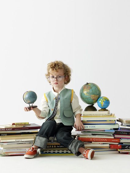 a young boy sitting on top of a pile of books with globes in front of him