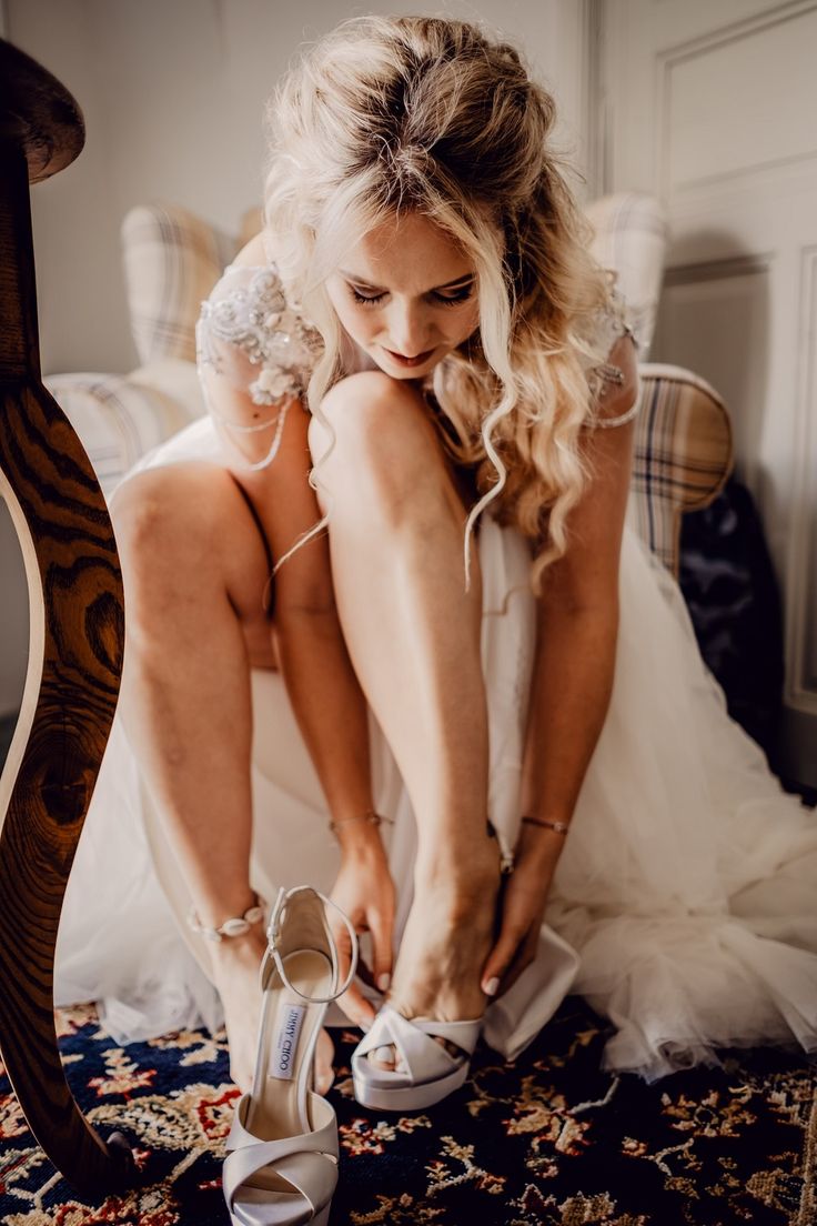 a woman sitting on top of a bed next to a pair of white high heels