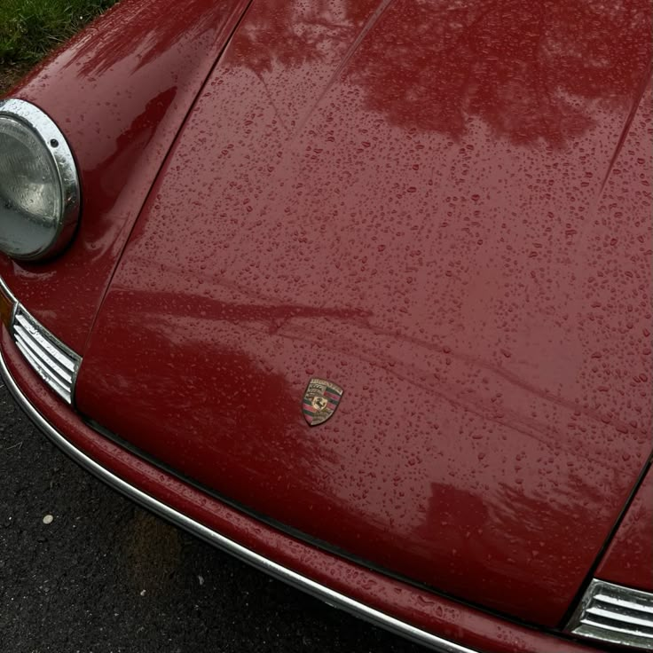 the front end of a red sports car with rain drops on it's hood